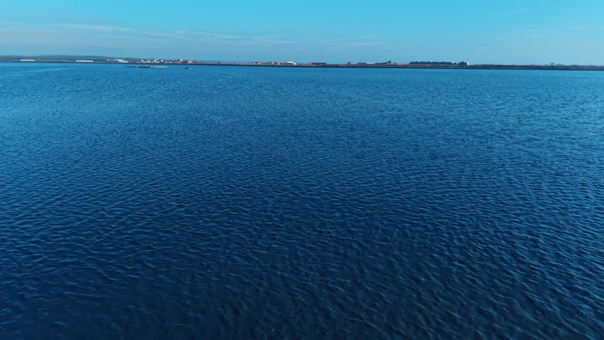 Empty calm blue water surface with distant land horizon. Wide landscape view of a blue lake with a low horizon line and clear sky.