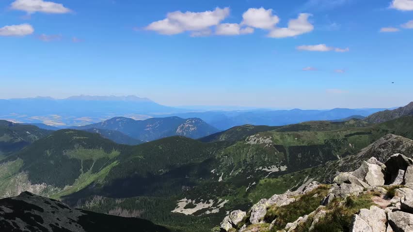 Stunning panoramic view from a high mountain peak on a sunny summer day. Green hills and rocky slopes stretching to the horizon under a blue sky in Demanovska Dolina, Slovakia