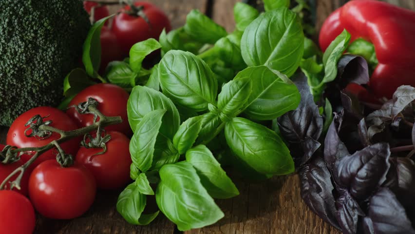 Fresh raw vegetables and herbs background. Broccoli, bell pepper, tomatoes and basil on wooden table. Plant based meal, healthy vegan food.