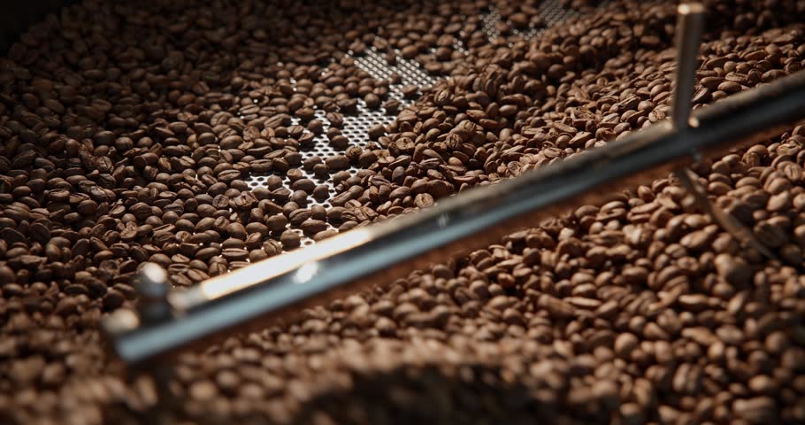Slow motion coffee beans tumbling and stirring inside industrial roaster production facility.