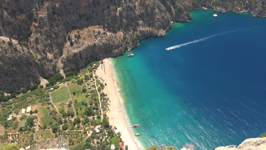Aerial view shows Butterfly Valley beach in Fethiye Mugla Turkey beside turquoise sea. White sand green gorge and steep cliffs create dramatic Mediterranean cove scenery. The view adds strong search relevance for geography, environment, scenic travel, and natural landscape storytelling with clear terrain definition.
