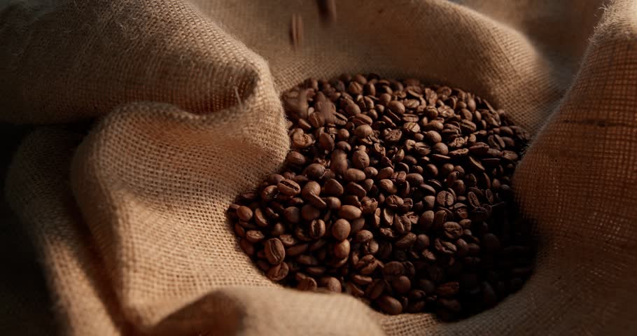 Slow motion coffee beans pouring into burlap sack on rustic table in kitchen.