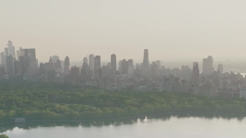 Looking across the water of the Central Park Reservoir toward the distant Manhattan skyline through a layer of summer morning mist.