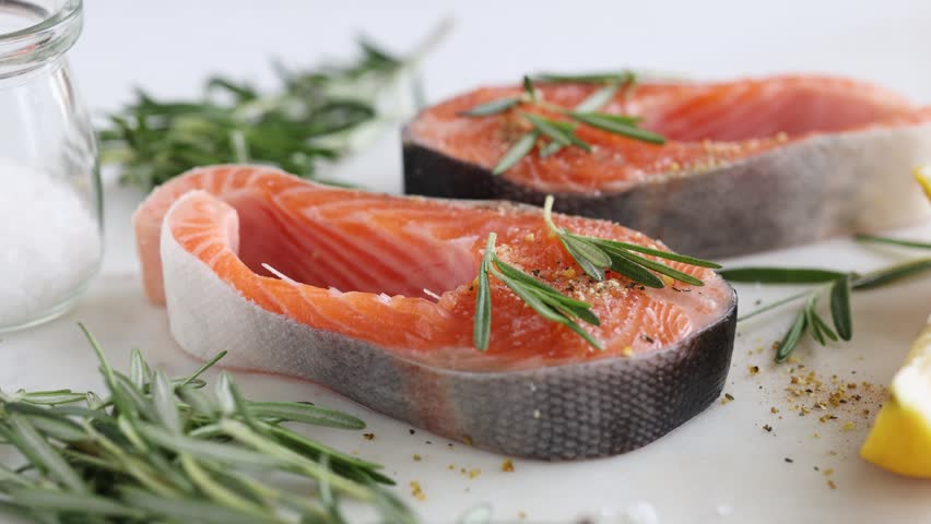 Pouring olive oil over raw salmon steaks before grill. Cooking process, healthy food