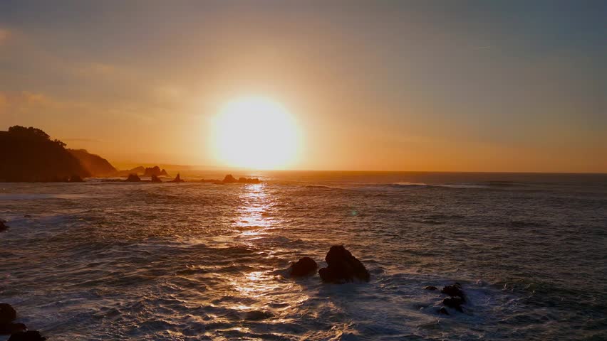 Sun setting over ocean horizon with rocks emerging from water.