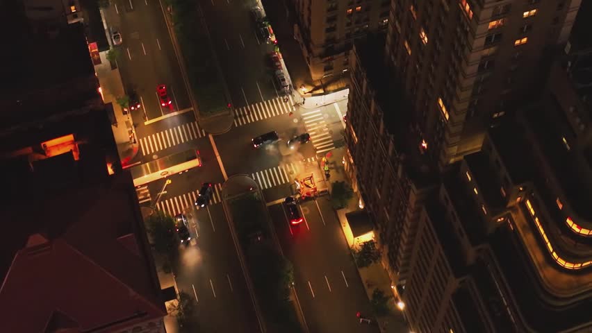 A high-angle top-down aerial view capturing the flow of traffic and yellow taxis on a bright Manhattan avenue with dark rooftops.
