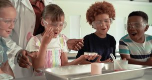 Diverse children watching teacher guiding child pouring red liquid into tray demonstrating science. Classroom, students, curiosity, foam, experiment, instructor, goggles - Powered by Shutterstock - Get 15% off with code: PIKWIZARD15