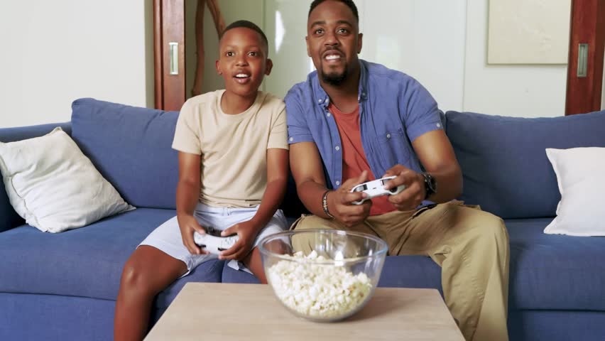 Dad and son gaming, game-triggered HUD overlays appearing, dad shielding son, holding controllers. Family, parent, stock, campaign, cozy, realistic, livingroom