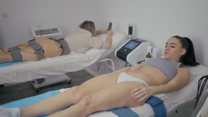 Two women receive body treatments in a modern beauty salon. Clients enjoy aesthetic procedures for skin and body shaping.