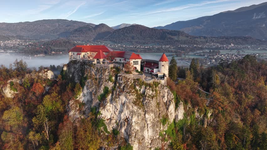 Red roofs cover the medieval Bled Castle on a cliff in Slovenia. Aerial drone shot reveals the town and mountains near Lake Bled, Slovenia