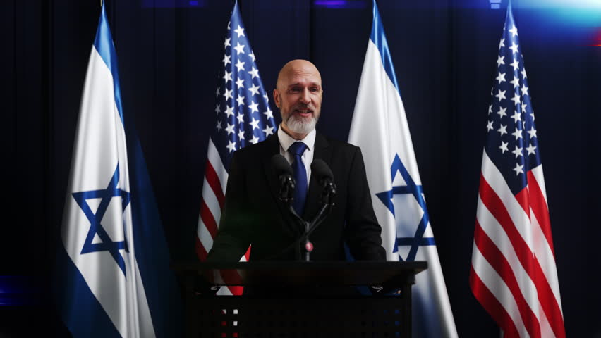 Male official making announcement with US and Israel flags on TV screen