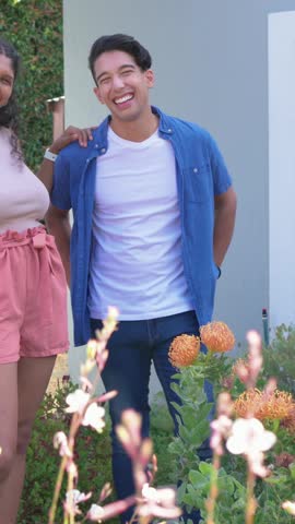 Vertical video: Laughing man, blue tee, reacting to woman touching shoulder in yard, orange blooms. Couple, garden, outdoor, candid, smiles, affection, vertical video