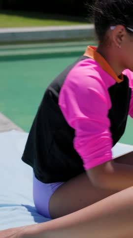 Vertical video: Sun urging girl in rash top fixing goggles, dabbing stick, mom rubbing legs at pool. Child, parent, lotion, towel, backyard, outdoors, vertical video