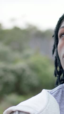 Vertical video: Starting man dreads wearing hoodie gray shirt turning right at park, copy space. Dreadlocks, outdoor, nature, foliage, bokeh, contemplative, vertical video