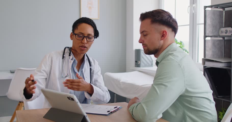 Doctor consulting patient during hospital appointment, consultation in modern clinic. Woman explaining diagnosis on tablet screen, talking to man about next steps of treatment plan, disease prevention