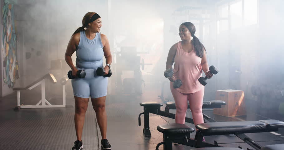 Diverse female friends greeting, lifting hex dumbbells, curling and pressing overhead in gym. Fitness, workout, strength, camaraderie, activewear, wellness, exercise