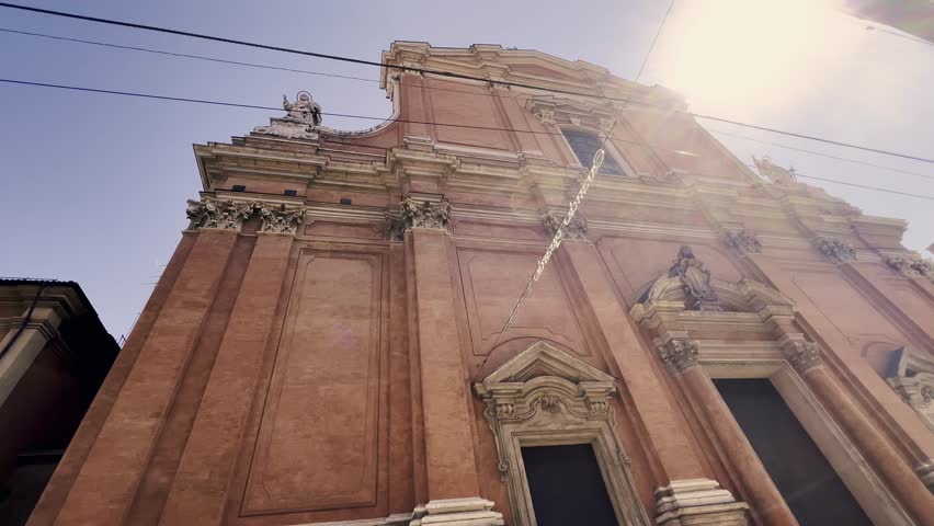 Low angle view of the ornate baroque facade of the Oratory of San Filippo Neri in Bologna, Italy, with the sun flaring brightly and the Garisenda Tower visible in the background