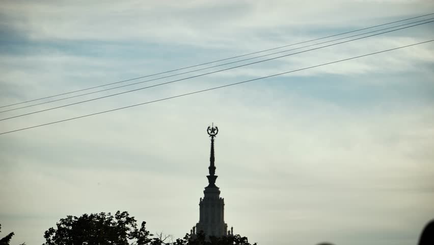 Person ziplining over Moscow State University building against a cloudy sky