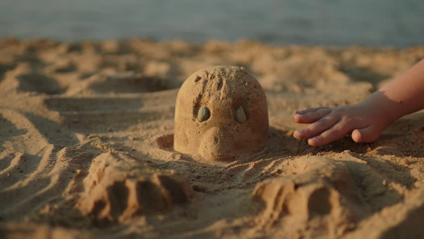 Child building sand statue on beach, closeup. Boy touching and moving sand grains with palm and fingers. Natural outdoor massage and early sensory development.