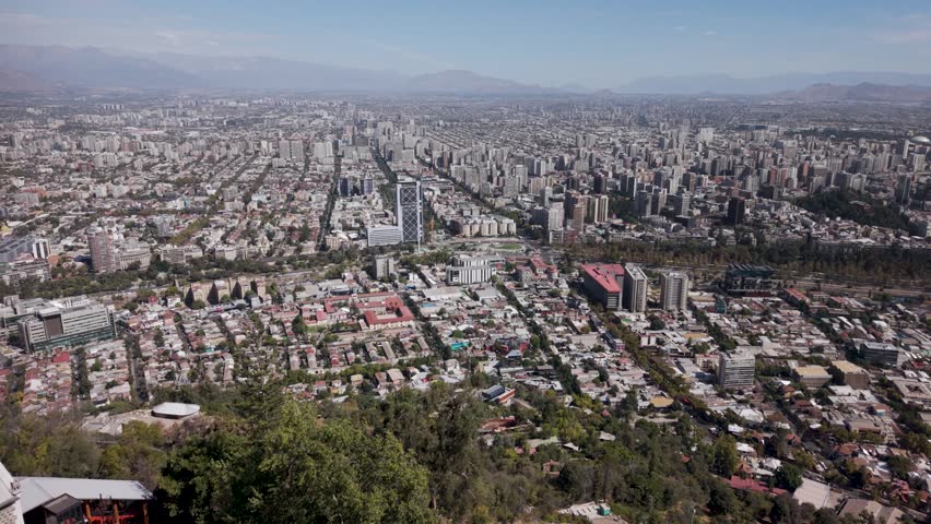 Aerial forward-moving shot capturing the expansive Santiago skyline and urban landscape as seen from the summit of San Cristóbal Hill, Chile