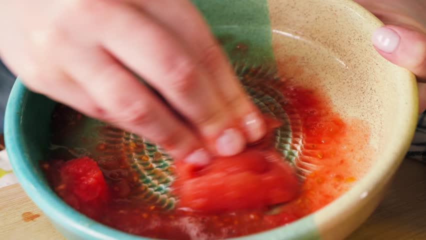 Close-up of hands grating fresh tomato on a traditional Spanish ceramic grater plate over a bowl for preparing pan con tomate. Natural tomato pulp made using a special dish plato rallador. High