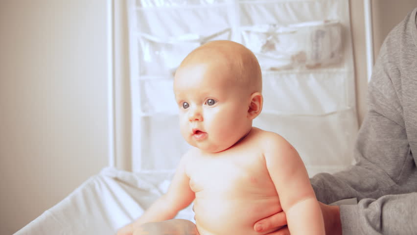 Happy newborn baby with blue eyes sitting on white bed sheets and looking around