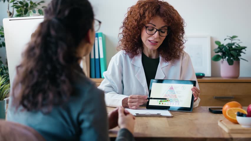 Video of nutritionist woman explaining the food pyramid to a patient using a digital tablet in a hospital consultation