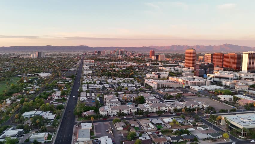 Aerial view of North 7th Street stretching toward the downtown skyline with office buildings and distant mountains under a soft sunset sky in Phoenix, Arizona, United States.