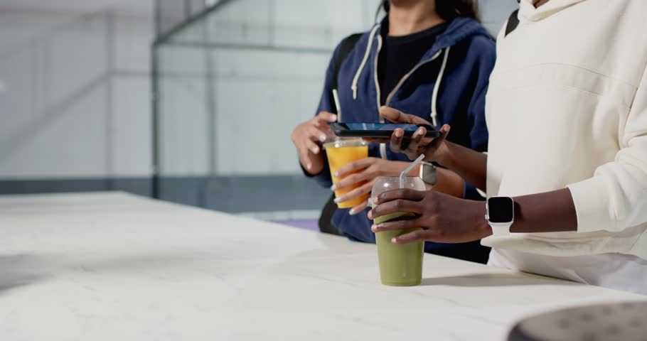 Diverse female friends placing phone on juice and smoothie cups, sharing workout progress at gym. Fitness, friendship, wellness, camaraderie, technology, casual, vibrant