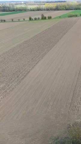 Vertical aerial view of expansive farmland with brown cultivated field and distant green parcels. Rural spring landscape.