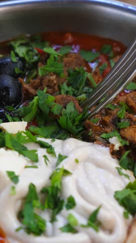 Mouthwatering closeup of a traditional mediterranean meal being eaten with a fork, featuring stewed meat, vegetables, black olives, feta cheese, and fresh parsley, served with warm flatbread