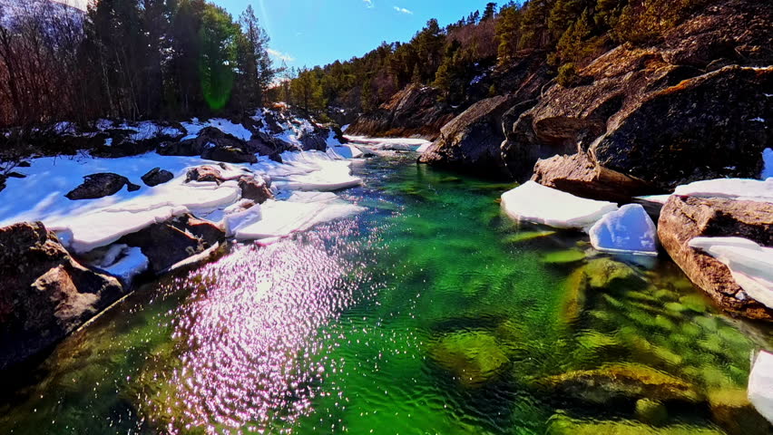 Crystal clear emerald river with sunlight reflections and visible stones beneath the water. Beautiful natural scene in northern Europe.