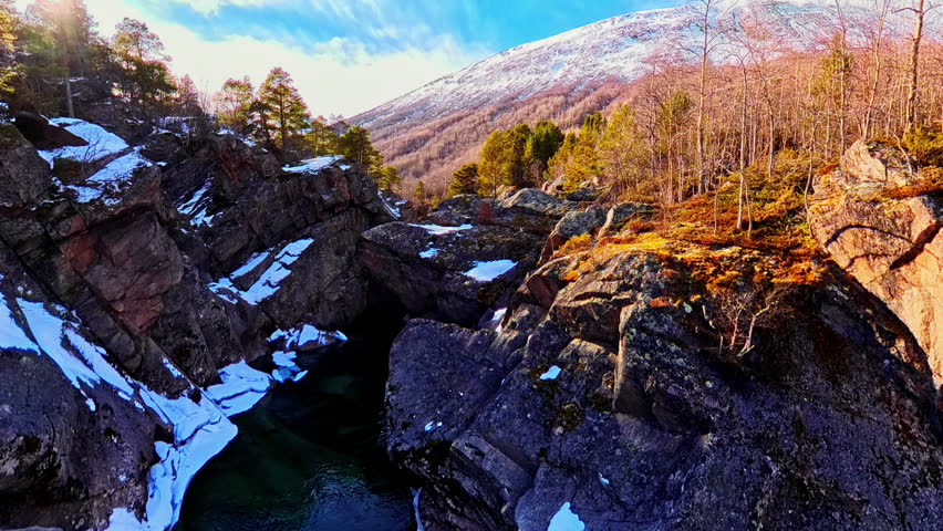 Sunlight shining over a rock canyon with a river below and patches of snow. Scenic natural landscape during early spring in northern Europe.
