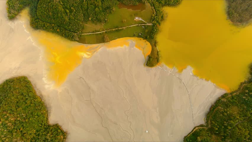 Aerial view of the toxic tailings pond with vibrant yellow and grey sludge surrounded by green forests at Geamana, Alba County, Romania.