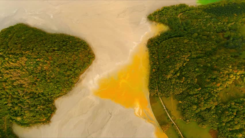 Aerial view of the toxic tailing pond with grey and yellow chemical sludge surrounded by green forested hills in Geamana, Alba County, Romania.