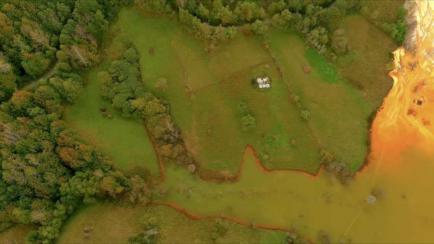 Aerial view of the toxic orange tailings pond flooding the green fields and surrounding forest of the sunken village Geamana, Alba County, Romania.