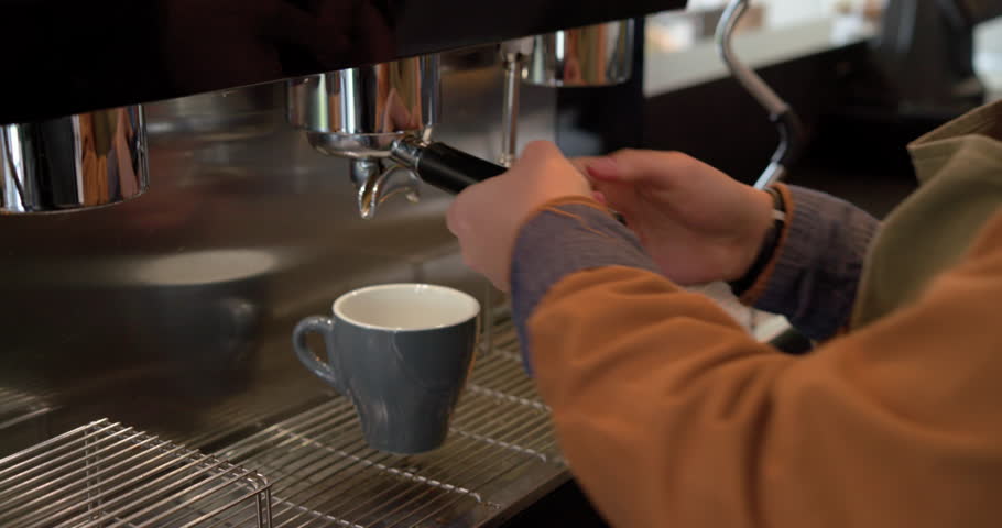 Barista locking portafilter under group head and pressing brew switch, extracting espresso into mug. Artisan, coffee, beverage, industrial, caffeine, barista, professional