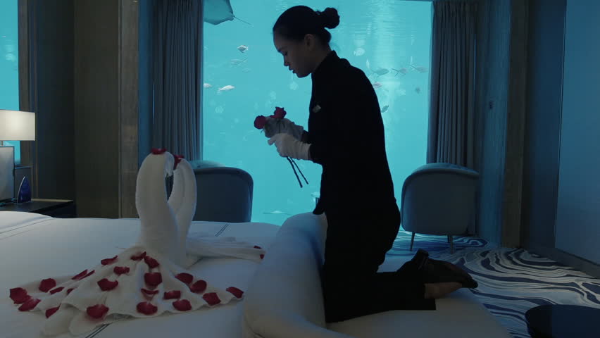 Room service preparing a romantic surprise with roses and towel swans in a luxury underwater hotel