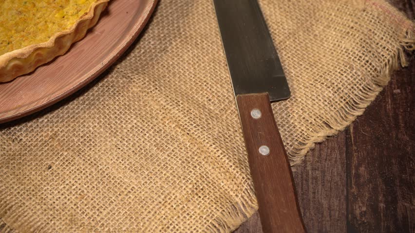 Cake on a plate with a knife, placed over a burlap tablecloth on a table.
