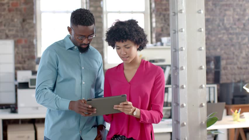 Pair holding tablet, man tapping, casting ghosted binary frames over tablet and bodies for business. Collaboration, colleagues, loft, daylight, glass, interface, digital