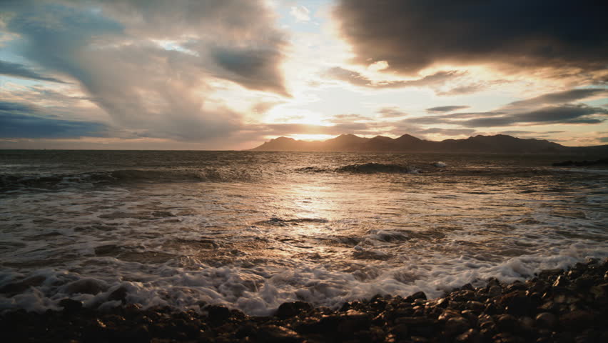 Evening waves washing over a rocky shoreline under dramatic clouds and warm sunset light