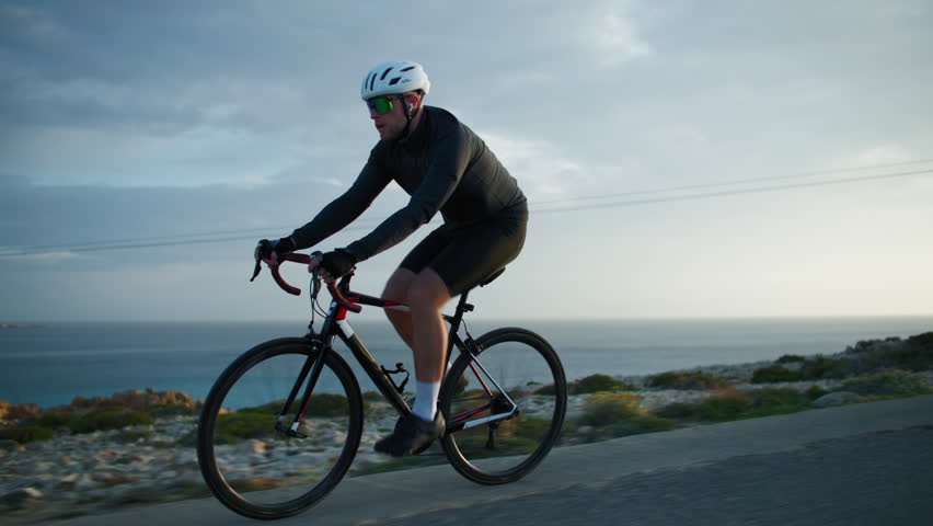 A guy. is practicing cycling while riding on the road near the sea. Sports and cycling in nature, workout and healthy lifestyle.