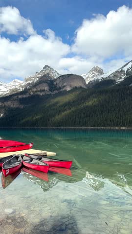 Red canoes moored on clear turquoise water reflecting snow capped mountains and green forest in Lake Louise, Banff National Park