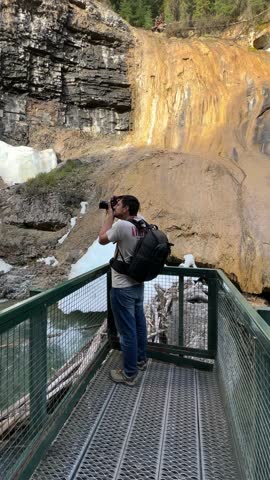 Male adventurer photographing a stunning waterfall with lingering snow in Banff National Park, Canada