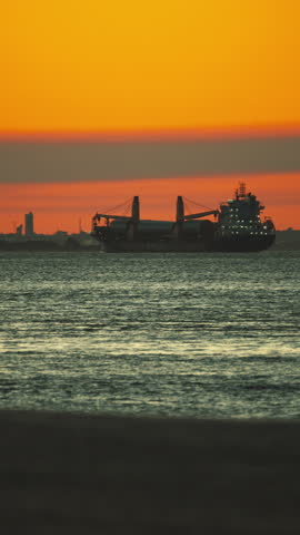 Large industrial cargo ship sailing on the sea with a beautiful orange sky during sunset