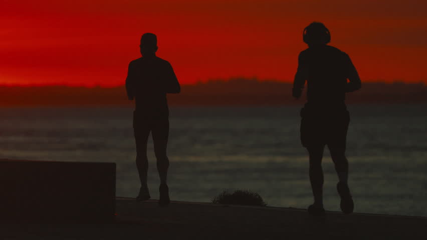 Athletic men jogging along the waterfront with a dramatic red sun rising over the sea