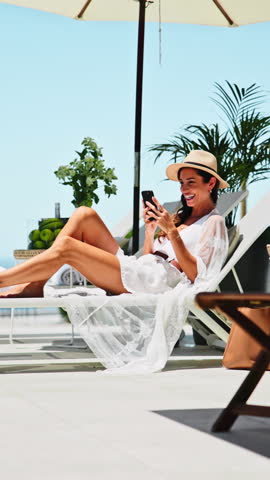 Woman, phone and laugh with deck chair for vacation, rest and relax for trip or break. Luxury resort, social media and person with travel, weekend and smile for hotel accommodation or hospitality