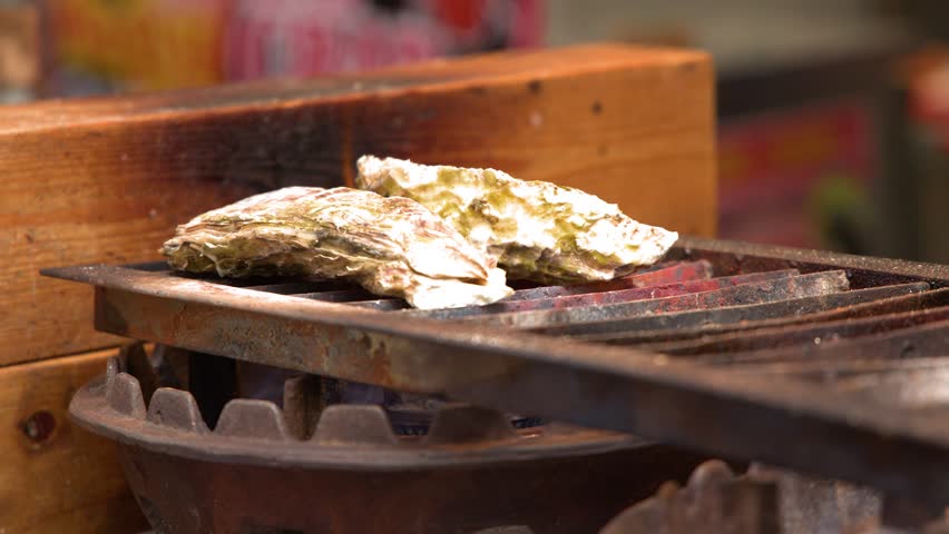 Close-up shot of two large oysters cooking over hot charcoal at a Japanese market
