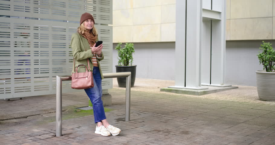 Senior couple leaning on railing in courtyard man tapping her scrolling phone and offering bouquet. Romance, connection, affection, companionship, outdoor, modern, serenity