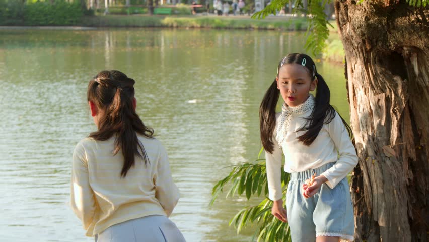 Two young girls throw food into a lake at Lumpini Park during golden hour sunlight